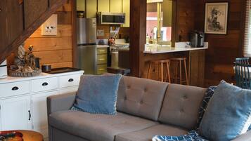 A cozy cabin interior with a sofa, kitchen area, and wooden walls.
