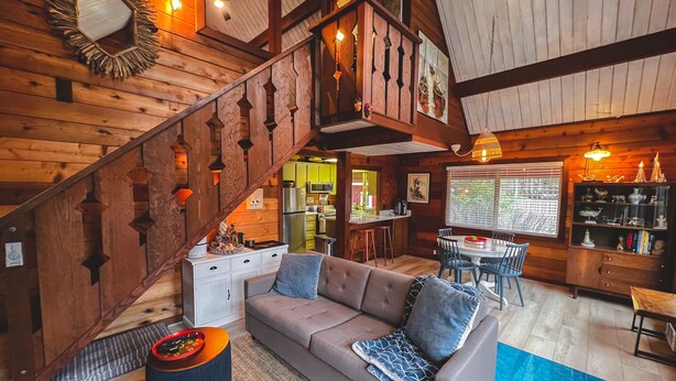 Interior acogedor de una cabaña con una escalera de madera, una zona de comedor y una sala de estar con sofá y mesa de centro.