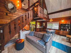 L’intérieur chaleureux d’un chalet avec un escalier en bois, un coin repas et un salon comprenant un canapé et une table basse.