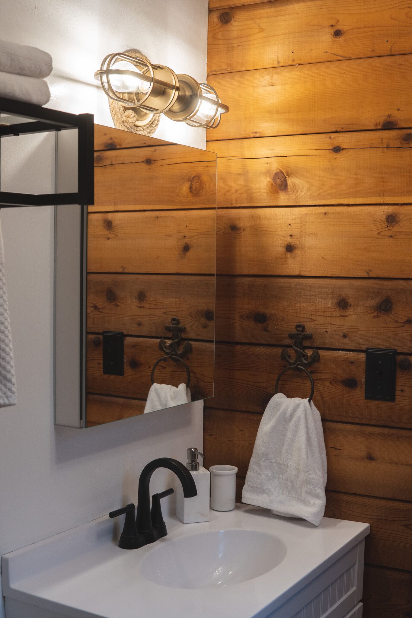 A bathroom with wooden paneling, a white sink, black faucet, and a mirror with a towel hanging on the wall.