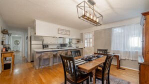 A modern kitchen with a central island, wooden dining table with chairs, and a chandelier.