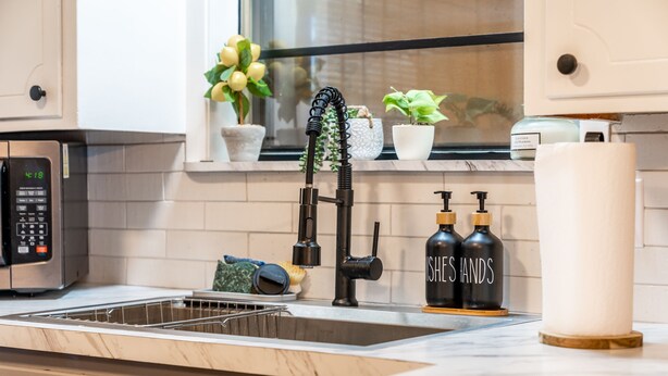 A modern kitchen with a built-in dishwasher, a black faucet, and a window with potted plants.