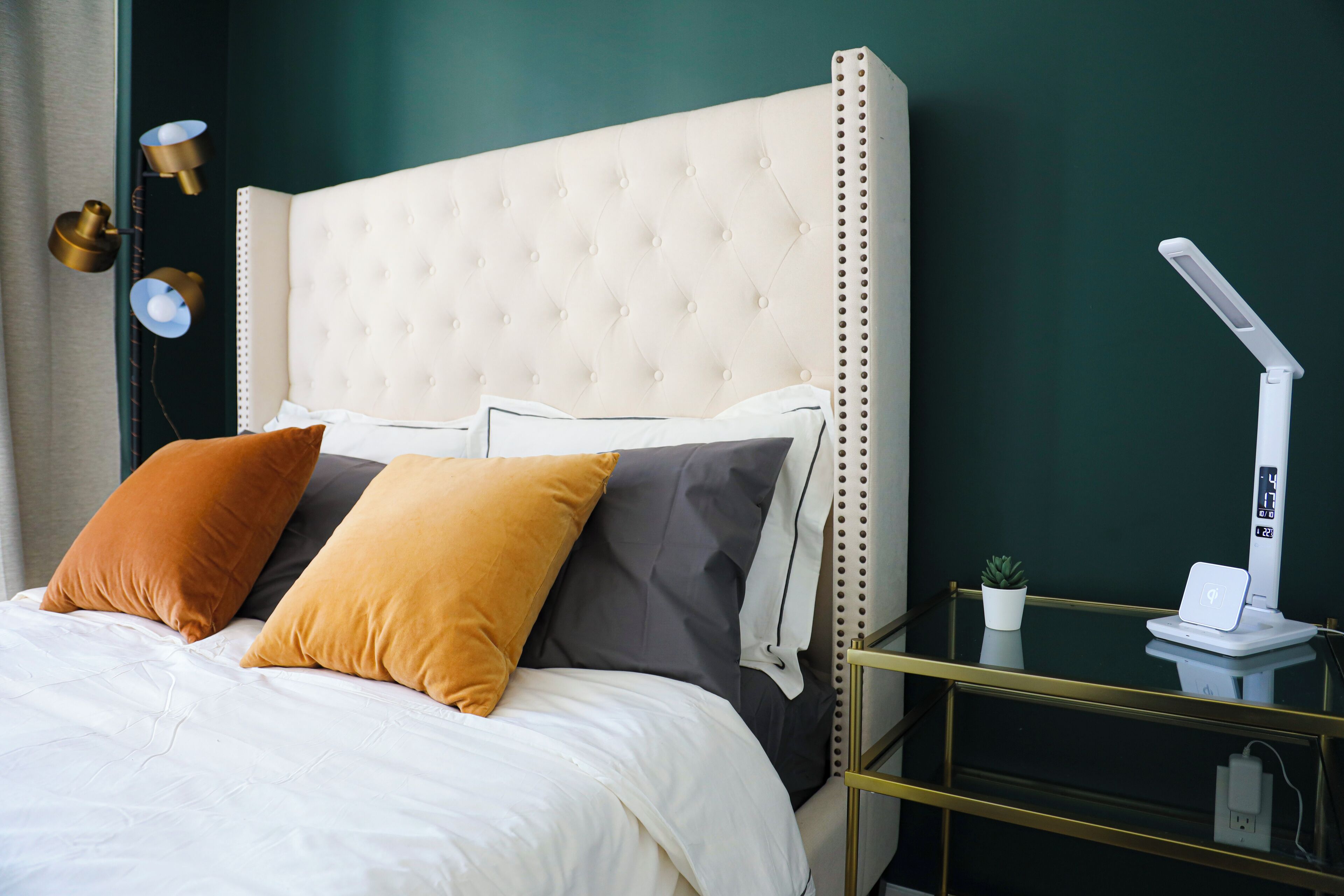 A neatly made bed with a tufted headboard, a bedside table with a lamp, and a small potted plant.