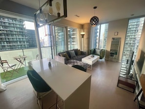 A modern living space with a sofa, coffee table, and dining area. Large windows offer views of a cityscape. - Spacious apartment in the heart of Toronto! Close to historic & touristic sites. (Toronto)