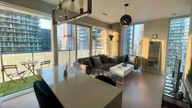A modern living space with a central island, seating area, and large windows offering city views.