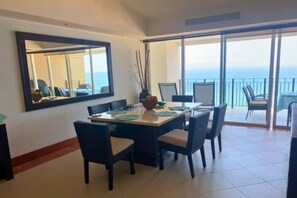 A dining area with a large table, chairs, and a view of the ocean through a balcony. - GRAND VENETIAN, OCEAN FRONT CONDO (PUERTO VALLARTA)