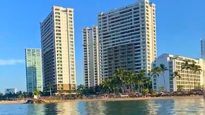 Un hotel frente a la playa con varios edificios altos, una playa de arena y palmeras.