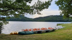 Une rangée de canoës et de kayaks était alignée sur une rive herbeuse, au bord d’un lac paisible, entourée d’arbres.