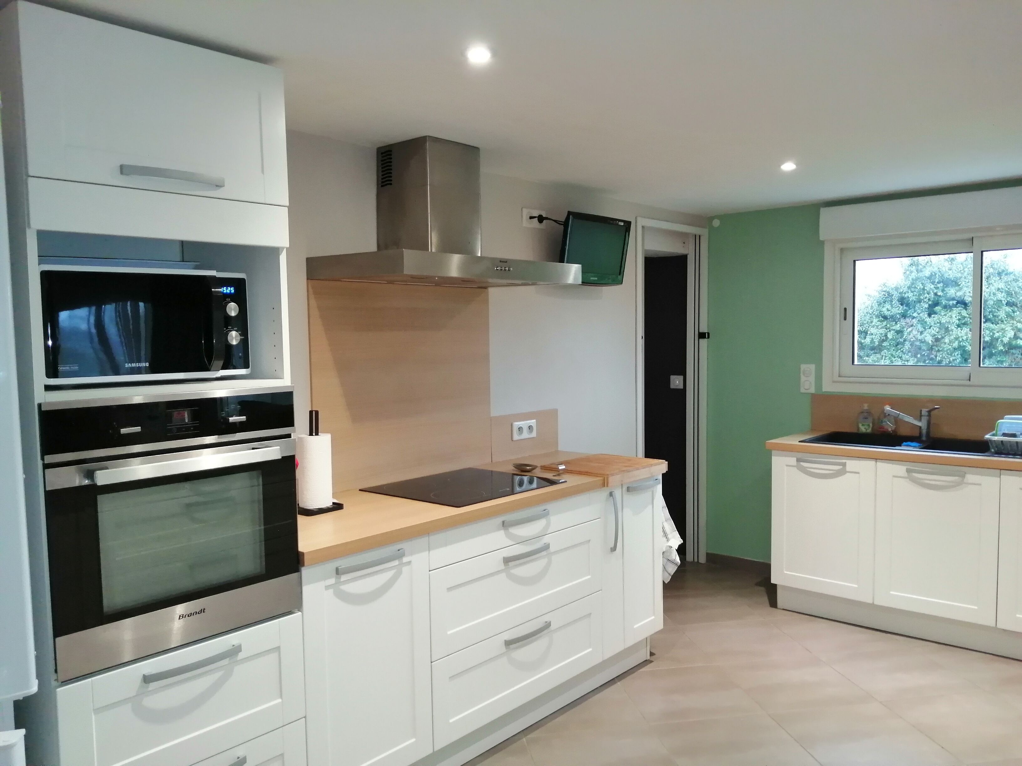 A modern kitchen with stainless steel appliances, white cabinetry, and a window providing a view of greenery outside.
