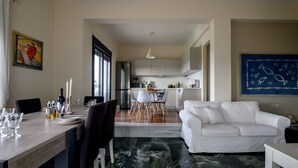 A modern kitchen with a dining area, a white sofa, and a marble floor. - Smaris Collection luxury villas.Sea side villa 5 min.from the beach ! (Σίσι)