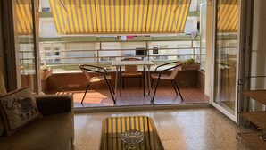 A balcony with a striped awning, a table with chairs, a cushioned sofa, and a wicker shelf. - Apartment l'Estartit (L'Estartit)