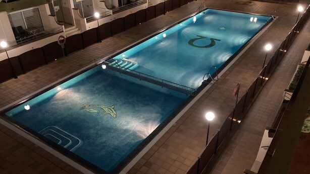 A rectangular indoor swimming pool with a dolphin logo, surrounded by a tiled walkway and a railing. - Apartment l'Estartit (L'Estartit)