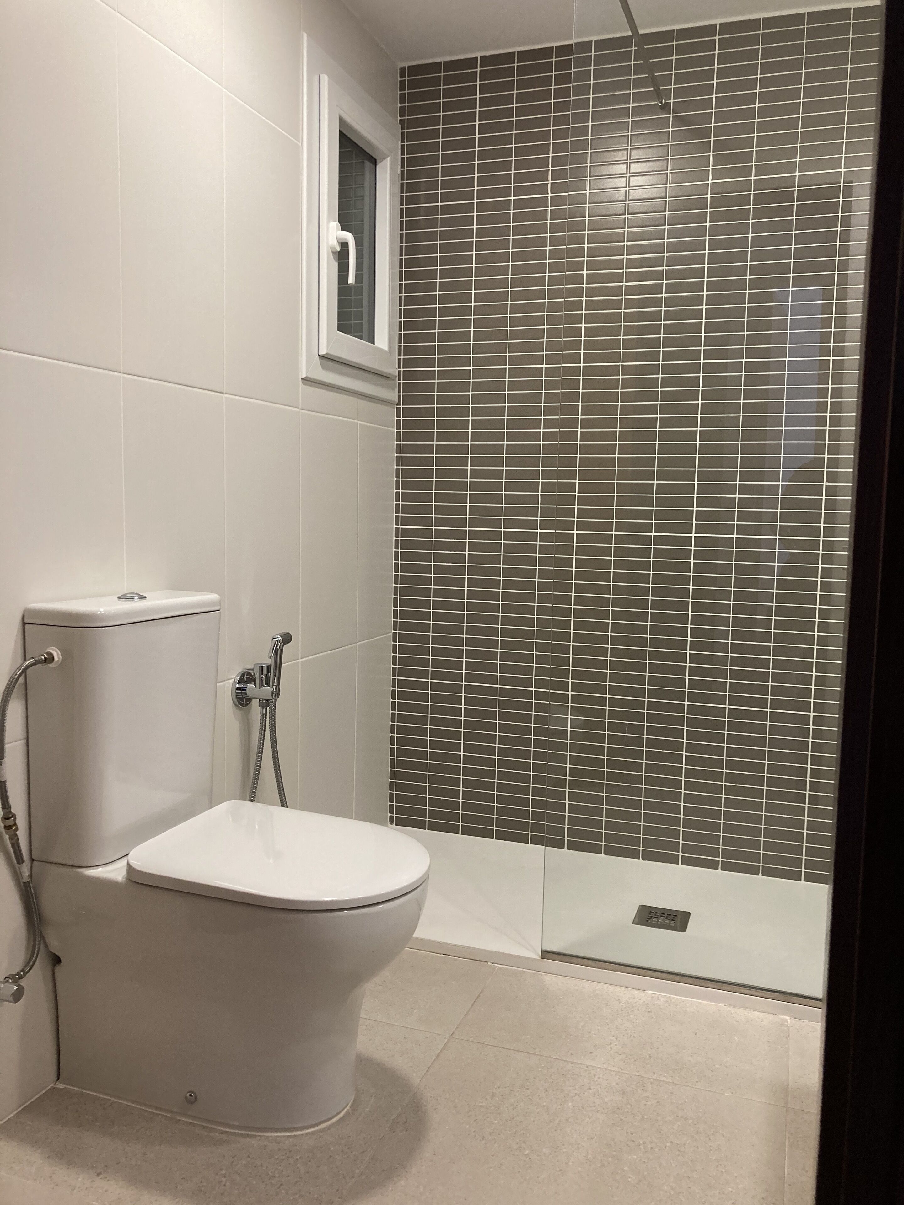 Un baño con inodoro, ducha y pared de azulejos.