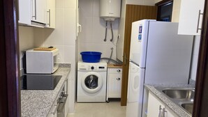 A compact kitchen with a washing machine, a refrigerator, and a microwave. - Apartment l'Estartit (L'Estartit)