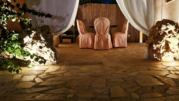 An outdoor seating area with stone flooring, pink chairs, and a rustic backdrop.