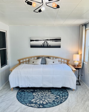 Une chambre avec un lit en bois, un tapis rond bleu à motifs floraux, un tableau accroché au mur et un luminaire fixé au plafond.