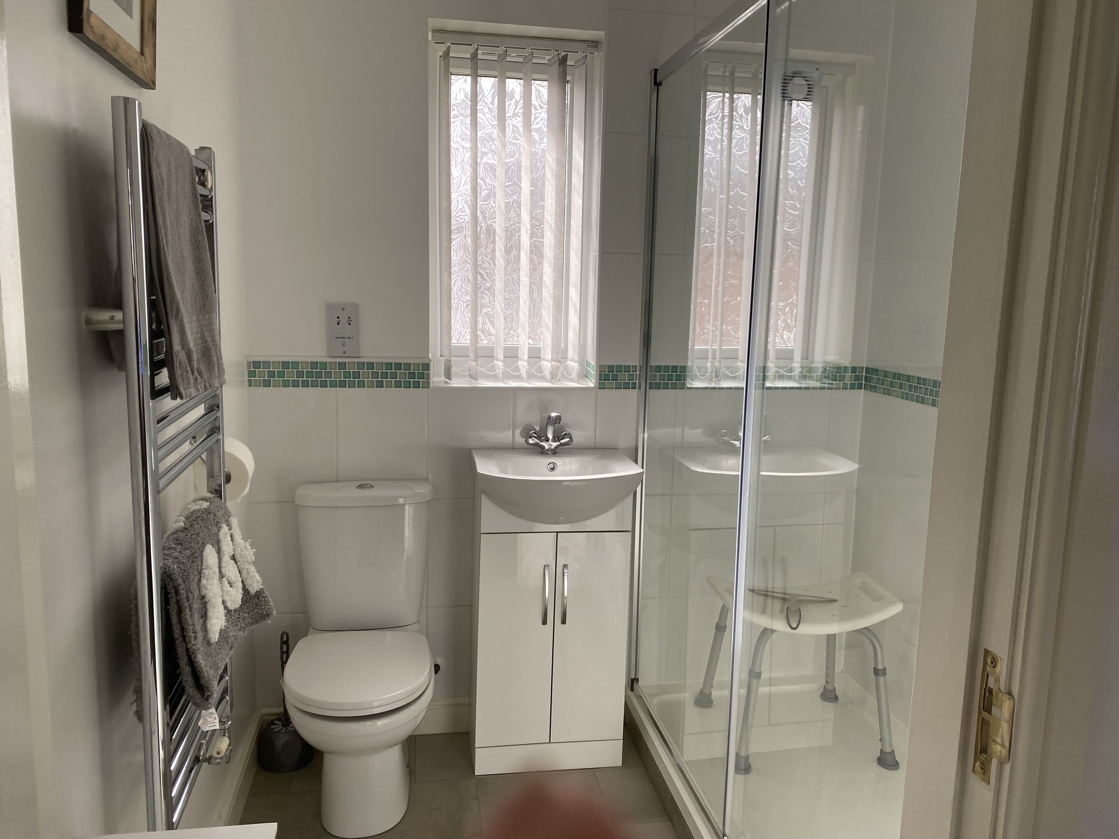 A bathroom with a toilet, a sink, a glass-enclosed shower, and a window with frosted glass.