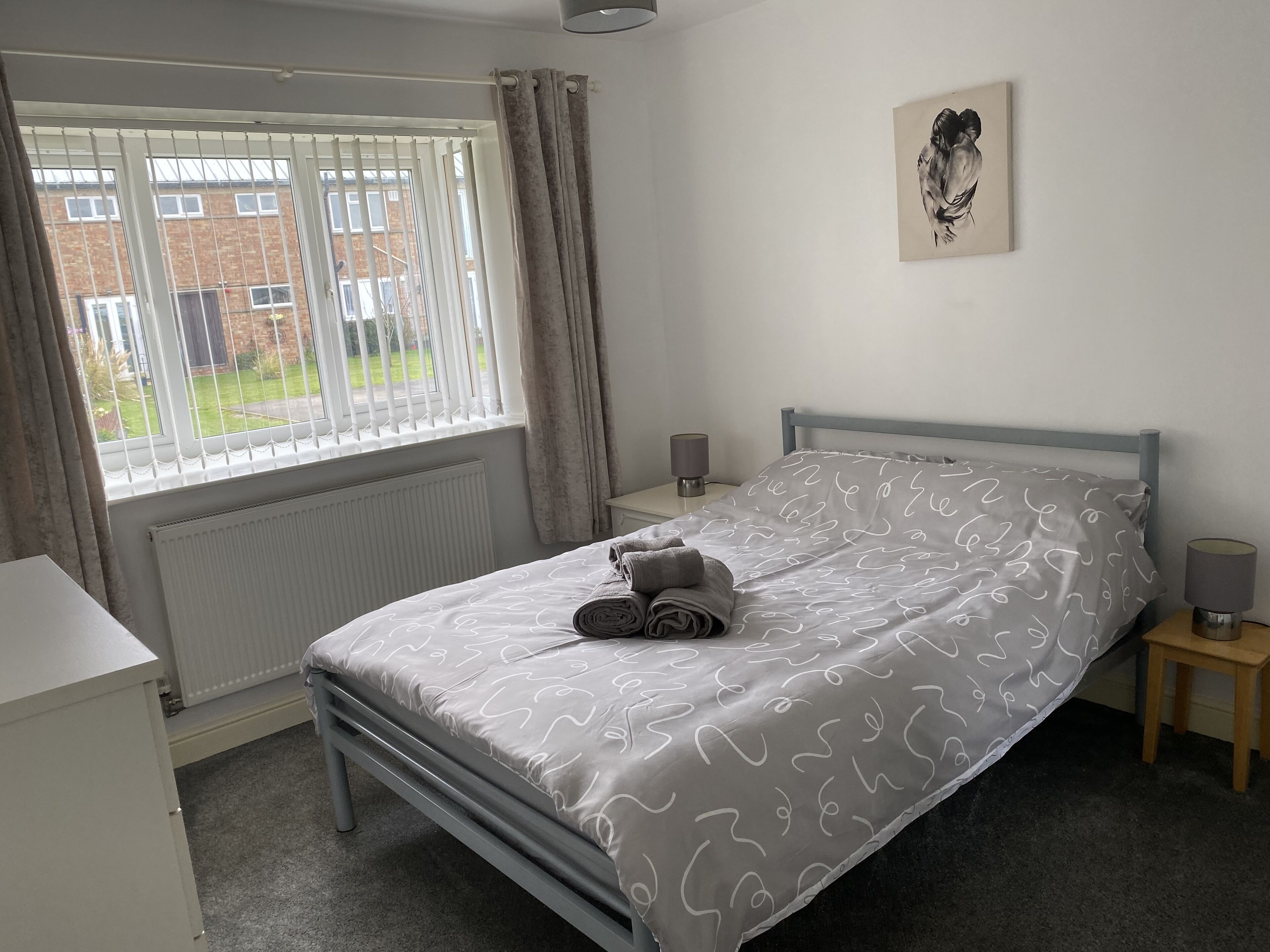 A neatly arranged bedroom with a bed, a bedside table, a lamp, and a window with curtains.