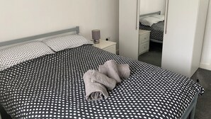 Un lit bien fait, avec une couvre-lit à pois, une lampe de chevet et un miroir au mur.