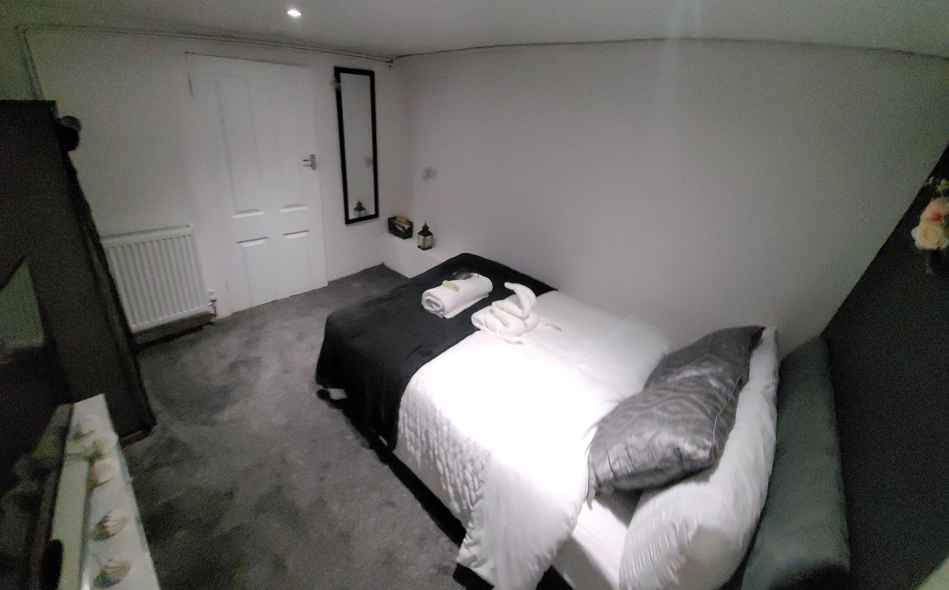 A small, dimly lit room with a single bed, a bedside table, and a mirror on the wall.