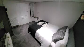 Una habitación pequeña con poca luz, una cama individual, una mesita de noche y un espejo en la pared.