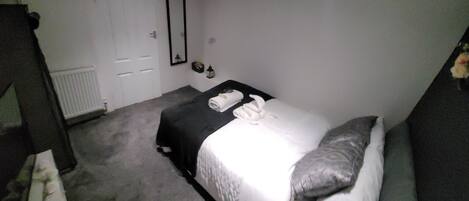 A small, dimly lit room with a single bed, a bedside table, and a mirror on the wall.