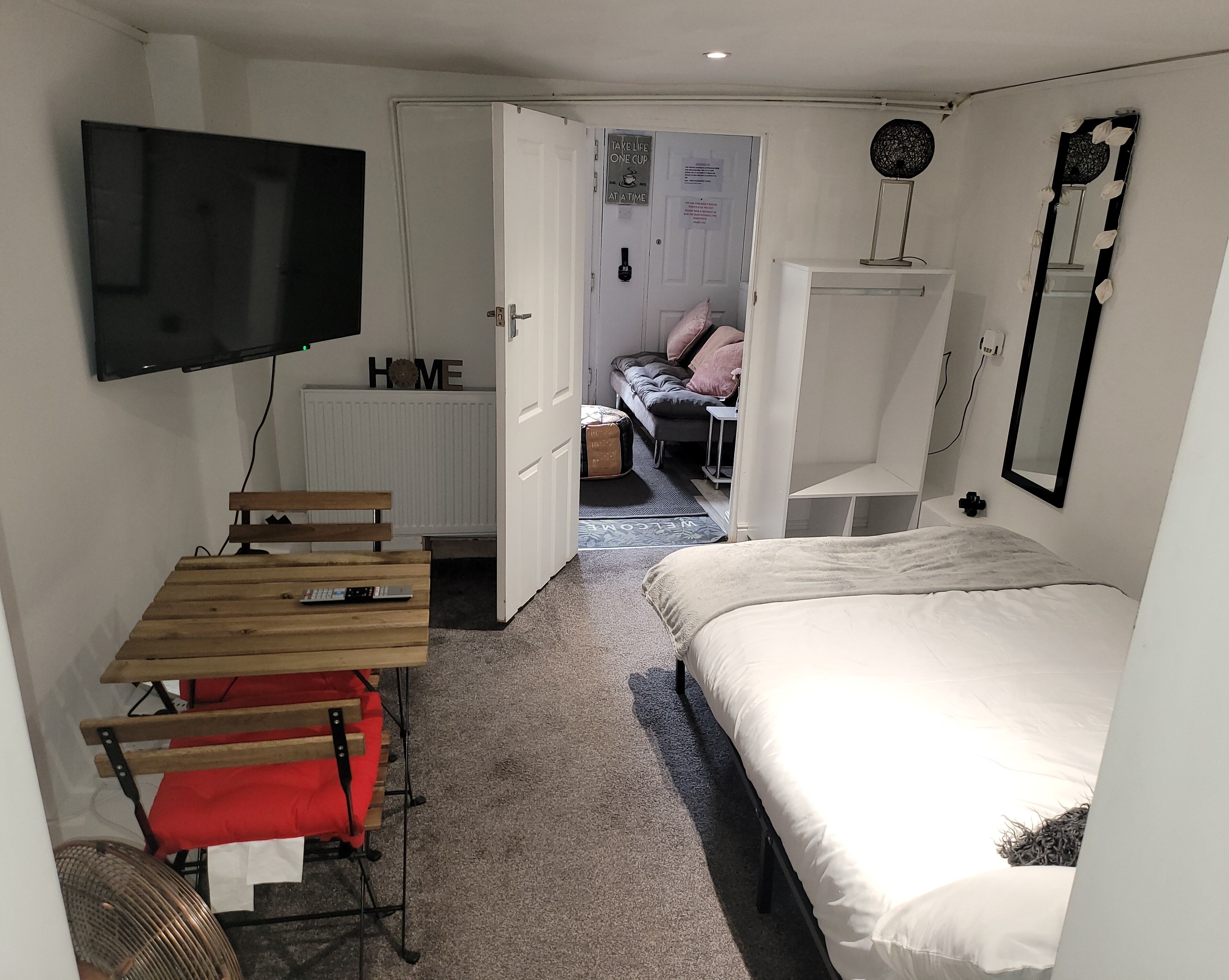 Habitació compacte amb un llit, una taula de treball amb una cadira, un televisor penjat a la paret i un armari.