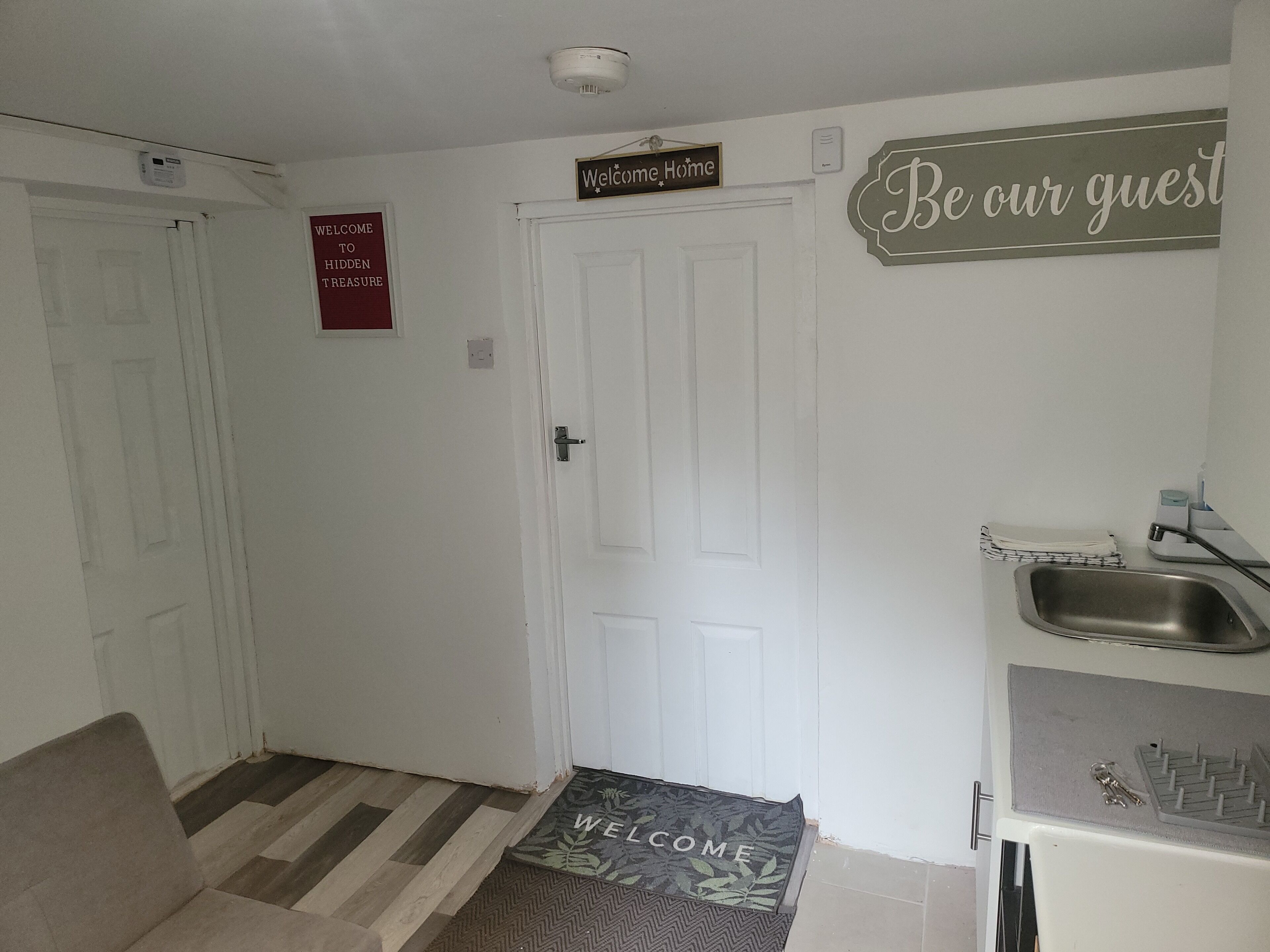 A hallway with a welcome mat, a sign reading "Welcome Home," and a sign saying "Be our guest."