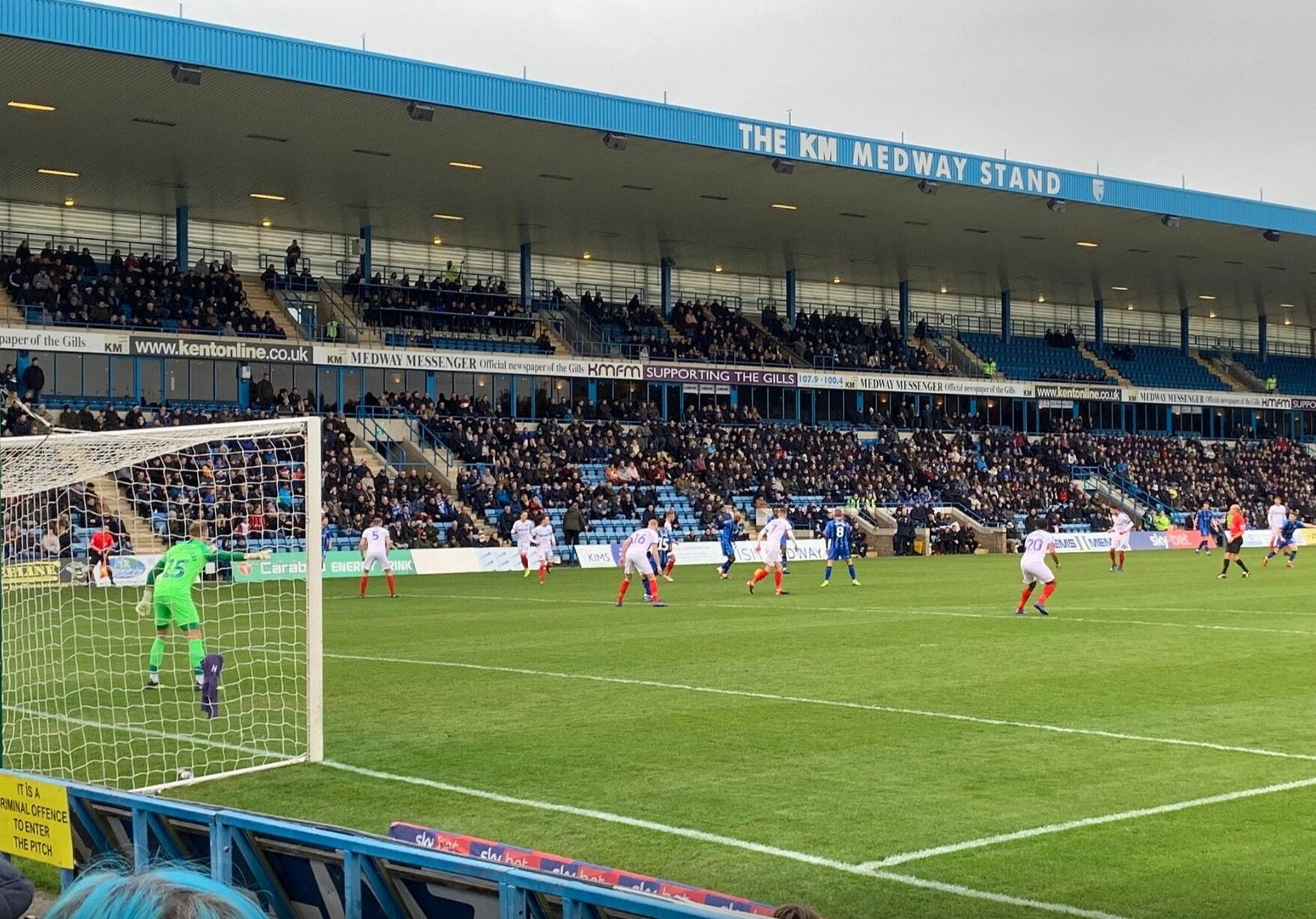 A football stadium with a large crowd, a goalpost, and players in action.
