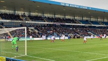 A football stadium with a large crowd, a goalpost, and players in action.
