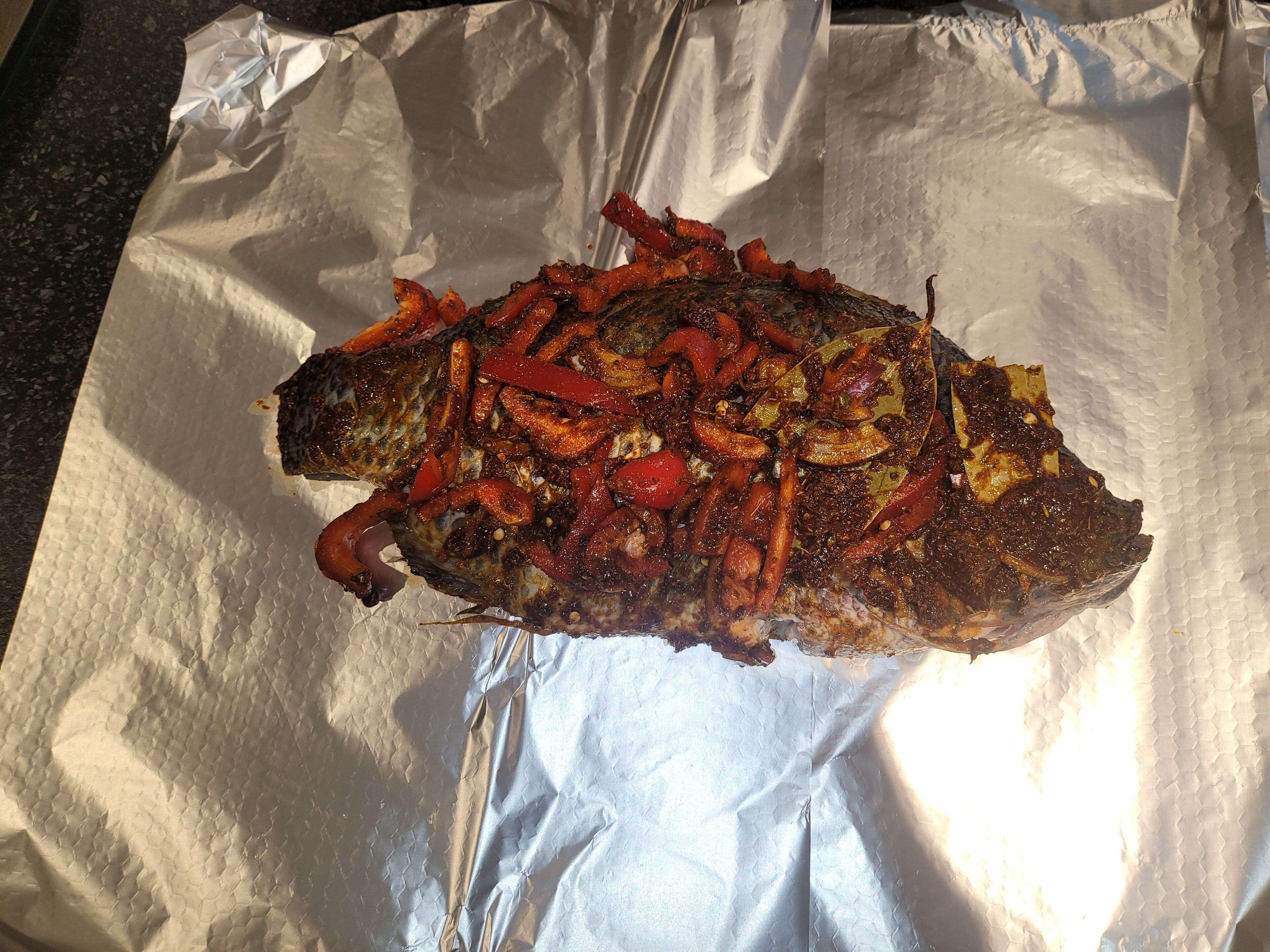 Un pescado entero con pimientos rojos y cebollas sobre papel de aluminio.