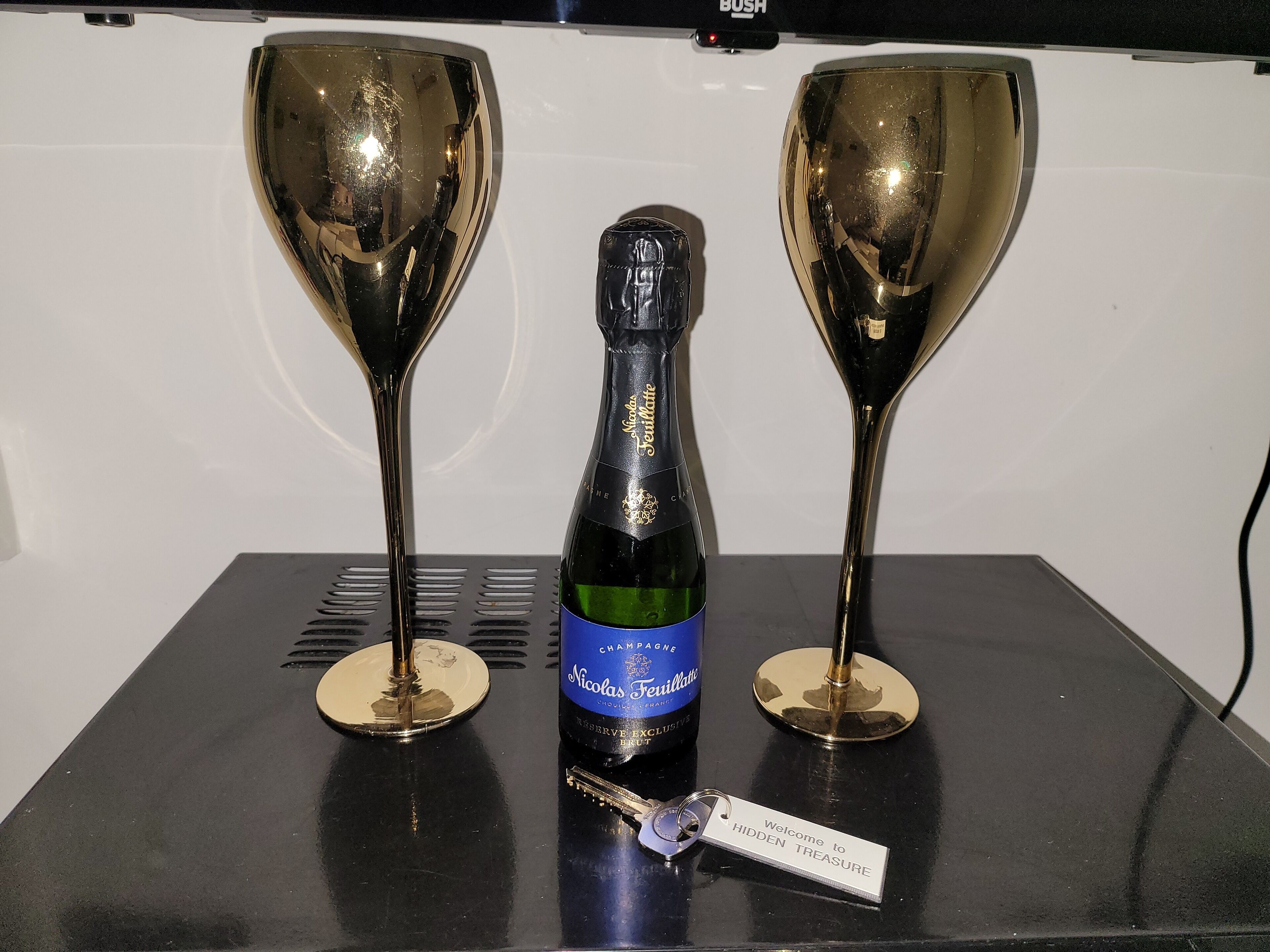 Een fles champagne met een blauw etiket en twee gouden wijnglazen op een zwarte tafel.