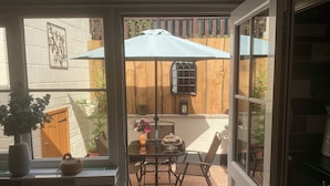 A patio area with a table, chairs, a vase with flowers, and a wooden fence in the background. - The Snuggery a Cosy Country Cottage (Wellington)