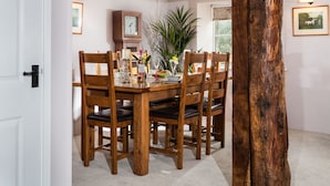 A dining area with a wooden table and chairs, a clock on the wall, and a large plant. - The Snuggery a Cosy Country Cottage (Wellington)