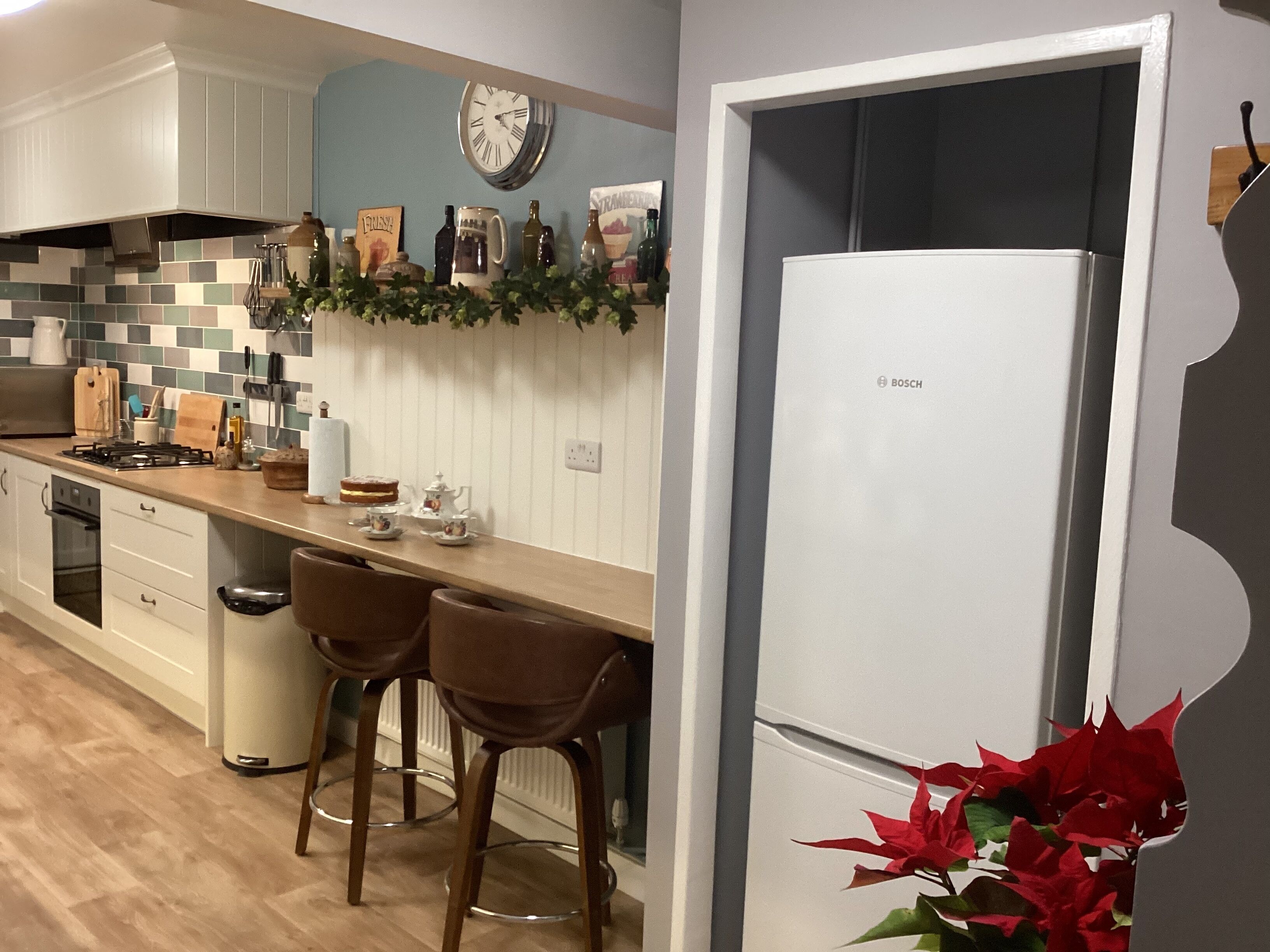 Una cocina moderna con armarios blancos, un refrigerador Bosch, un reloj y una pared decorativa con plantas.