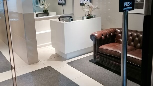 A reception area with a white counter, a brown leather couch, and a 'PUSH' sign on a pole. - Beautiful and Modern Apartment in North London (London)