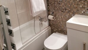 A bathroom with a glass-enclosed shower, a white toilet, and a sink with a tiled backsplash. - Beautiful and Modern Apartment in North London (London)