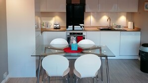 A modern kitchen with white cabinets, a stainless steel range hood, and a dishwasher. There is a glass table with two white chairs in front. - Beautiful and Modern Apartment in North London (London)