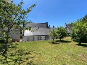 Ein Haus mit geneigtem Dach, einem kleinen Vorgarten und einem Baum.
