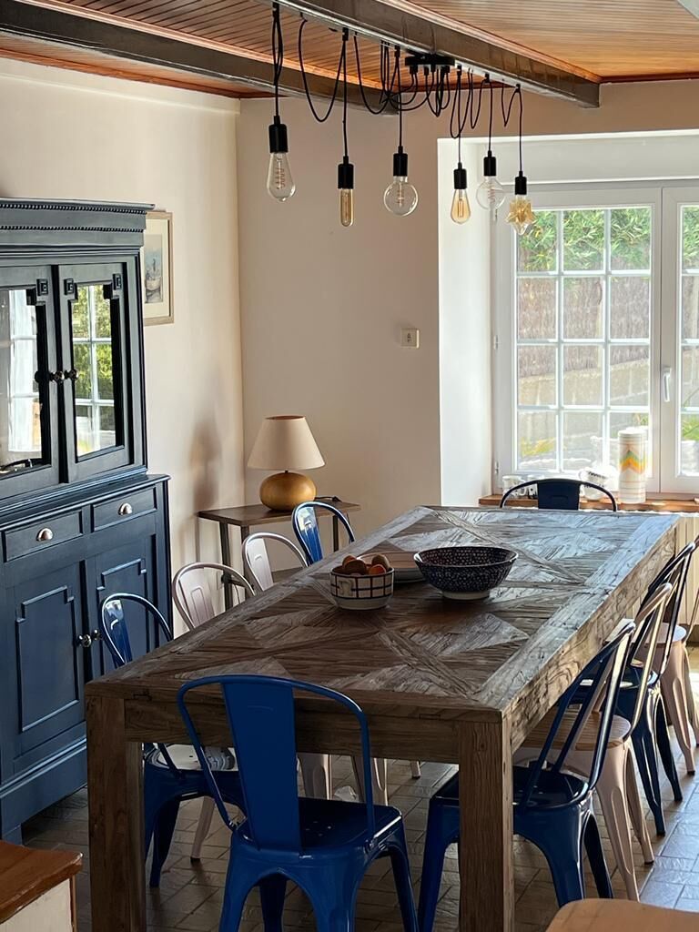A dining area with a long table, blue chairs, and hanging light fixtures.