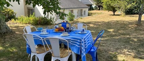 Een terras met een tafel voor vier personen, omringd door witte stoelen, onder een boom.