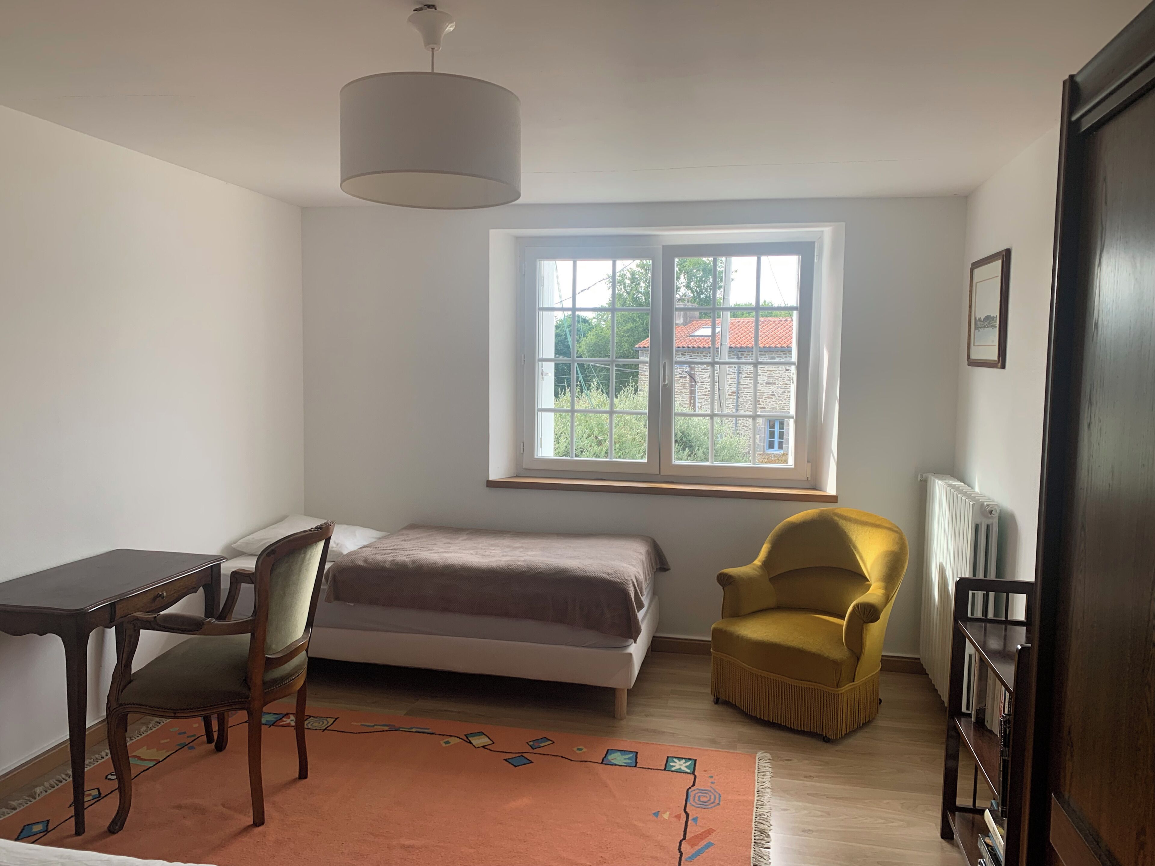 Une pièce comprenant un lit, un bureau, une chaise, une fenêtre et un radiateur.