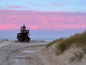 Ein Strand mit einer großen Metallkonstruktion, möglicherweise einem Leuchtturm, und Sanddünen.