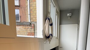 Une cuisine compacte comprenant un réfrigérateur, une petite table avec un pot de plante et une fenêtre avec un sac suspendu.