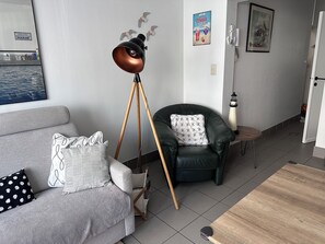 Un salon moderne avec un canapé gris, un fauteuil en cuir noir, une lampe sur pied et une petite table en bois.
