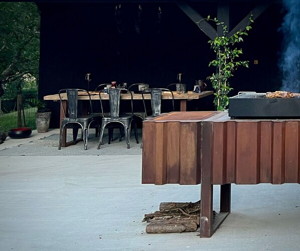 An outdoor dining area with a wooden table and metal chairs, a grill, and a potted plant. - Moulin des Arts (Loché-sur-Indrois)