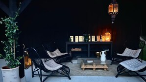 A cozy outdoor seating area with wicker chairs and a coffee table, a potted plant, and a lit fireplace in the background. - Moulin des Arts (Loché-sur-Indrois)