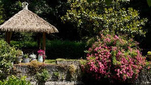 A thatched-roof gazebo surrounded by lush greenery and pink flowering bushes. - Moulin des Arts (Loché-sur-Indrois)