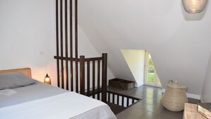 A bedroom with a bed, a nightstand, a lamp, a wooden chair, a woven basket, and a view of the outdoors. - Moulin des Arts (Loché-sur-Indrois)