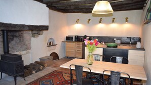 A rustic kitchen with a wood-burning stove, a dining table with chairs, and a vase of flowers. - Moulin des Arts (Loché-sur-Indrois)